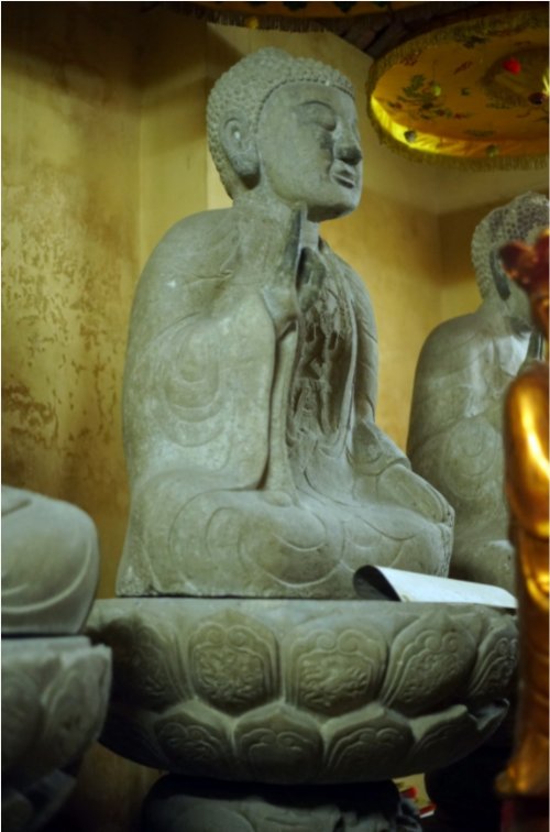 Bức tượng ở giữa được tạc trong tư thế ngồi thiền“bán kiết già” trên toà sen, tay phải giơ lên trong tư thế kết ấn, tay trái để úp nhẹ nhàng trên đùi trái. Tượng vận pháp y với ba lớp mềm mại: Lớp ngoài choàng qua bờ vai, lớp trong phủ kín toàn thân, lớp trong cùng phía trên để hở ngực đeo dây anh lạc.