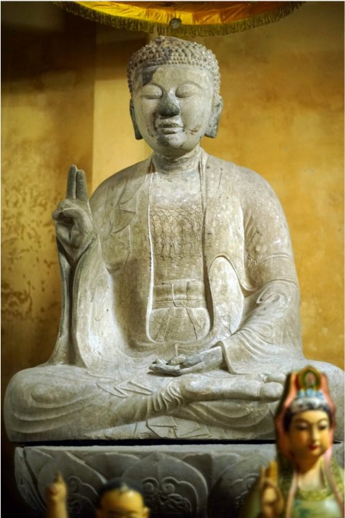 Tượng bên phải đượng tạo tác tương tự pho ở giữa, nhưng có đôi chút khác biệt trong tư thế ngồi thiền, thế tay kết ấn. Áo cũng có ba lớp, lớp ngoài choàng qua vai, lớp trong choàng kín người để hở cổ và ngực đeo dây anh lạc, trước bụng thắt “con ro”.